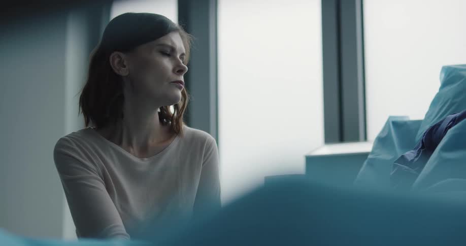 A woman sitting indoors gazing out of a large window on a cloudy day