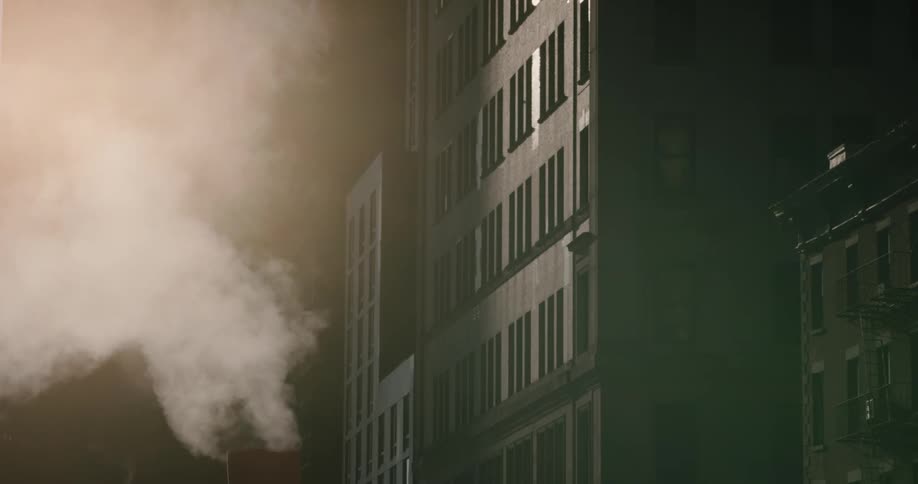 Smoke rises from chimney near taller buildings at night