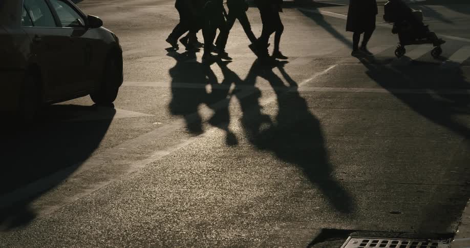 Multiple people and a baby stroller walk across a cross walk in front of a car