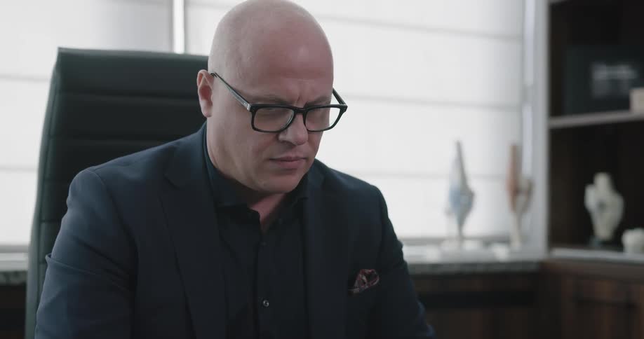 Bald man with glasses sitting at desk in office