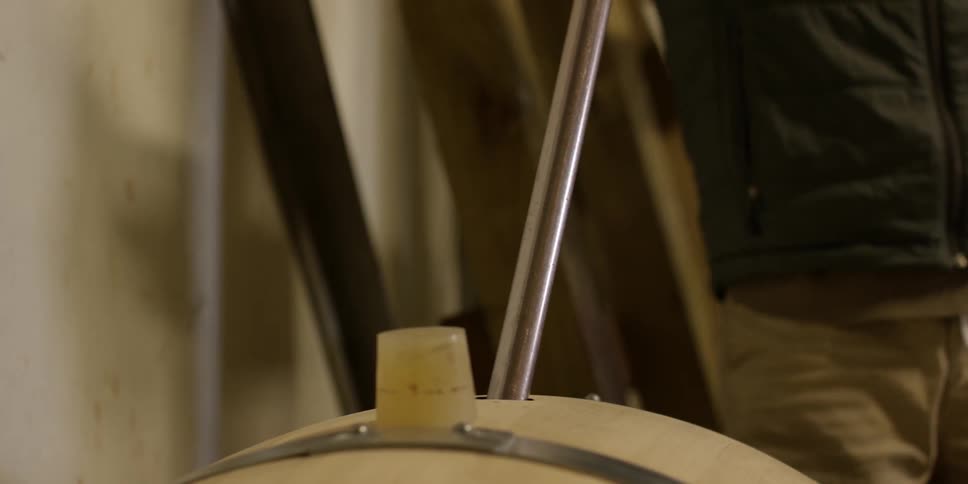 A long metal tube being placed in a wooden barrel