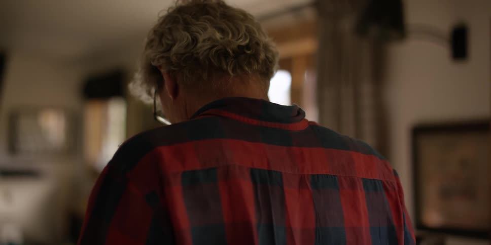 A older male standing in a house looking down and seen from behind