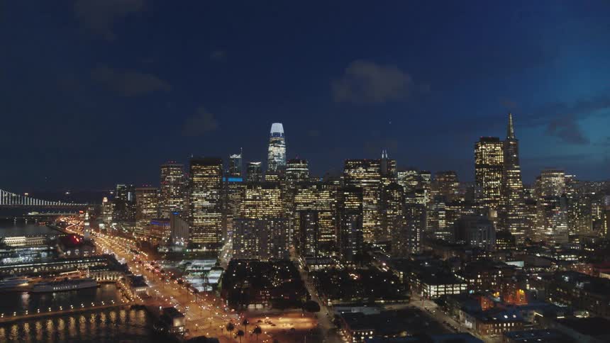 Traffic is driving past a metropolis that is illuminated at night