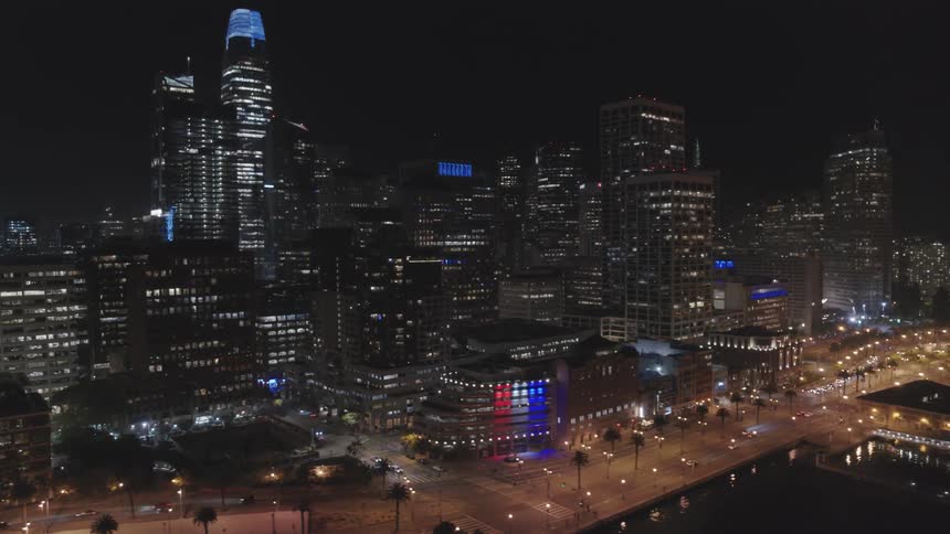 A skyscrapers top is illuminated at night in an urban area