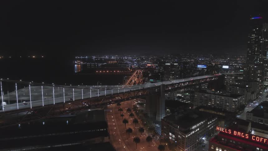 Vehicles travel a long bridge at night to the city
