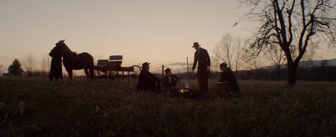 A group of cowboy sit in front of the camp fire