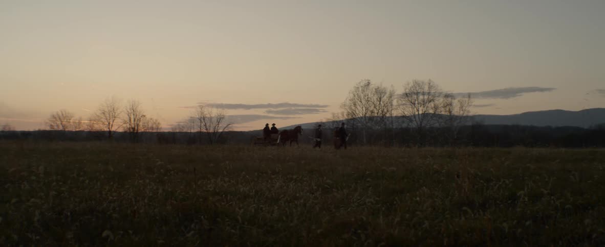 A group of people with a horse walk through a valley at sunset