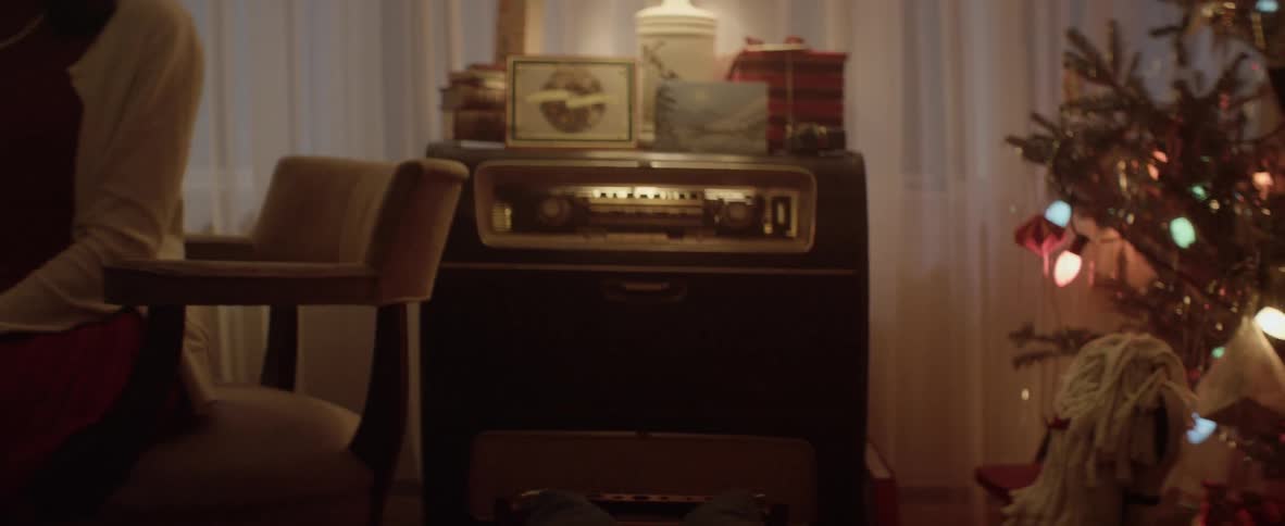 A woman sits in a chair next to a vintage radio and christmas tree
