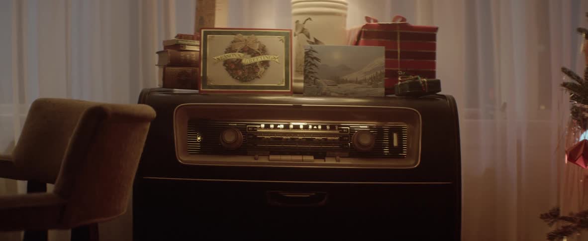 A person walking by a large radio with christmas cards a lamp and books on top