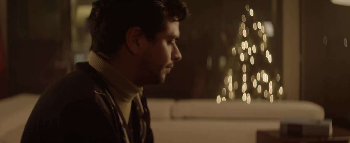 A man sitting in the living room with christmas tree lights in the background