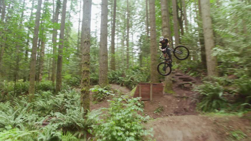 A person jumps their mountain bike off a ramp on the trail
