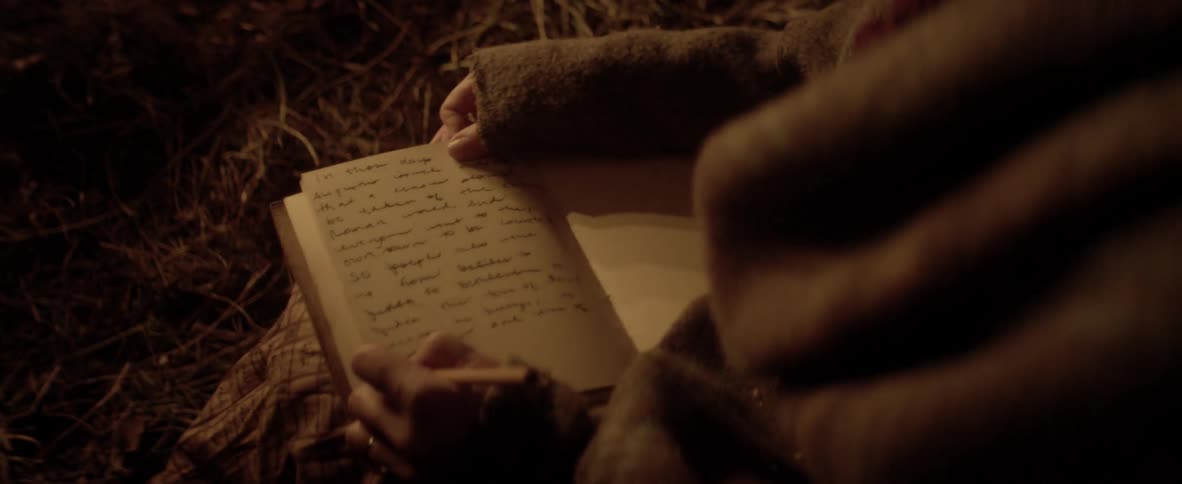 Woman writing in the book under a candle light at night