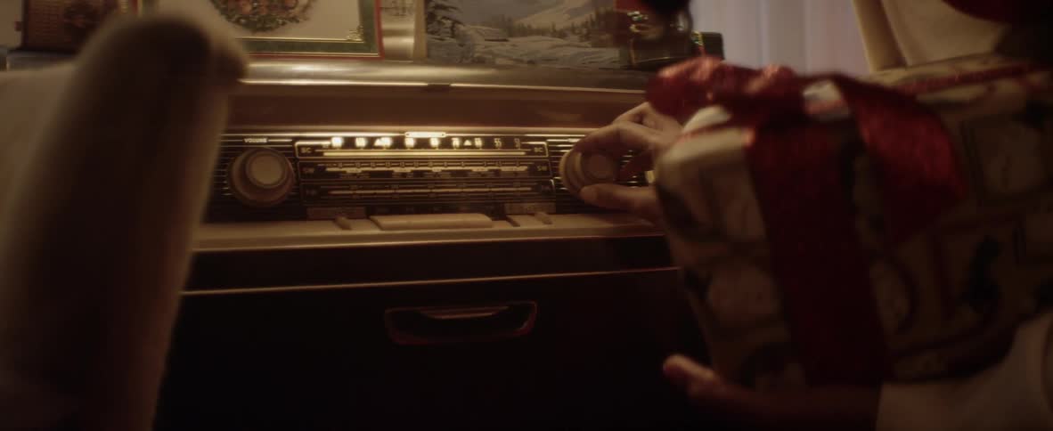 A woman carrying a wrapped gift stooping to adjust a jukebox