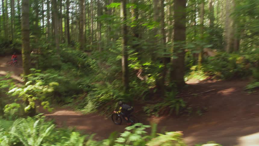 Mountain biker jumps over on the forest track in woods during daylight