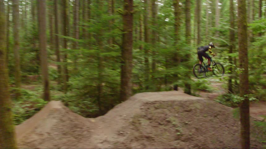 A man on a mountain bike ascends a ramp and soars through the air to land on the other side of the ramp in a forest