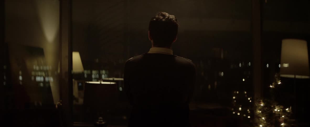A man walks towards the window and looks out in to the darkness