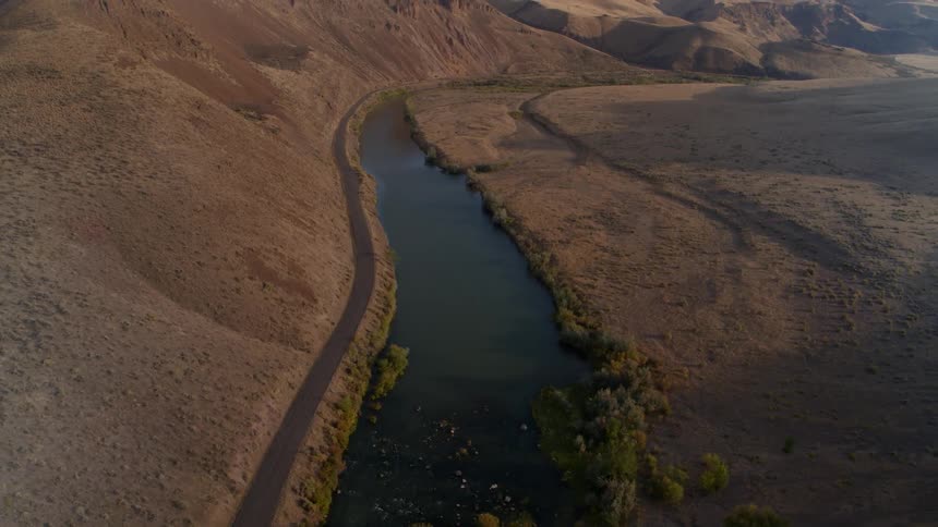 Shrubs grow along a river between desert sand dunes