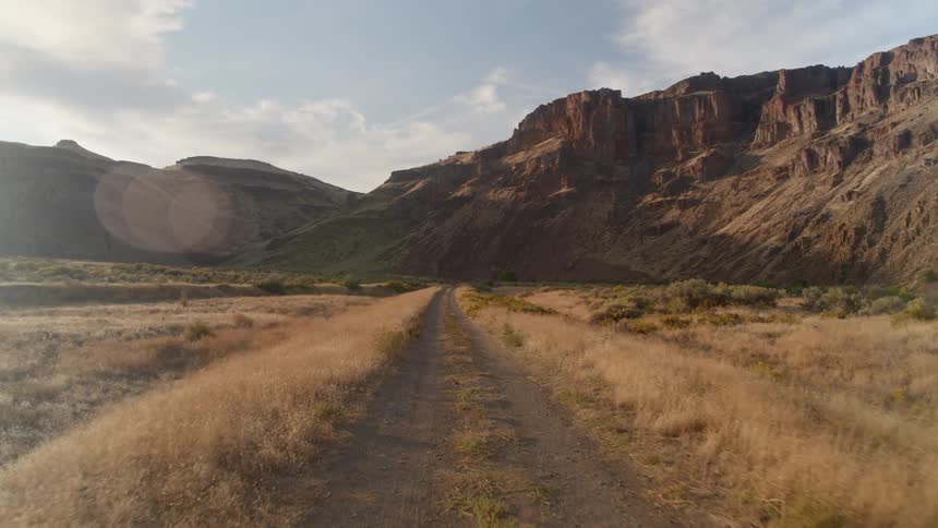 A straight path in the middle of dry brush and mountains in the distance
