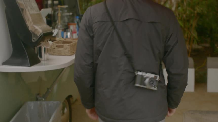 A man walks to a cafe with a camera strapped on him