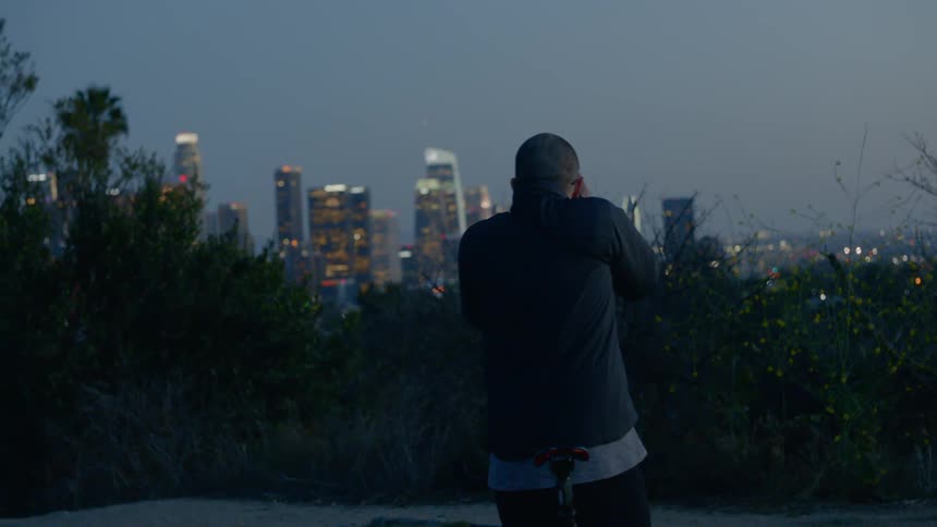 A young man bikes to look at the view of the city and then takes a picture at dusk