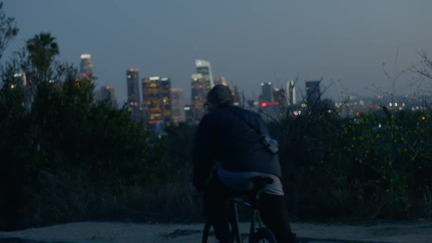Photographer on bike outside city at dusk observes the lights of the city skyline
