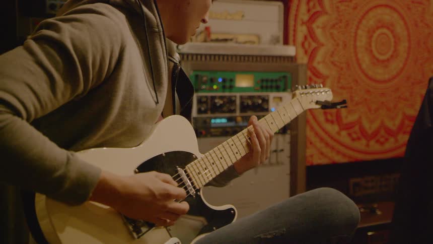 A young man sits with a cream colored guitar in his lap and hes moving his body slightly in time with the music