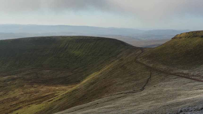 A trail runs across a grassy hill