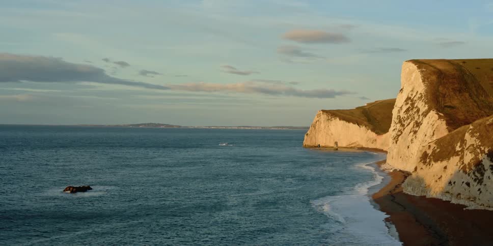 A coastal scene with steep cliffs and an outcropping of rocks in the sea
