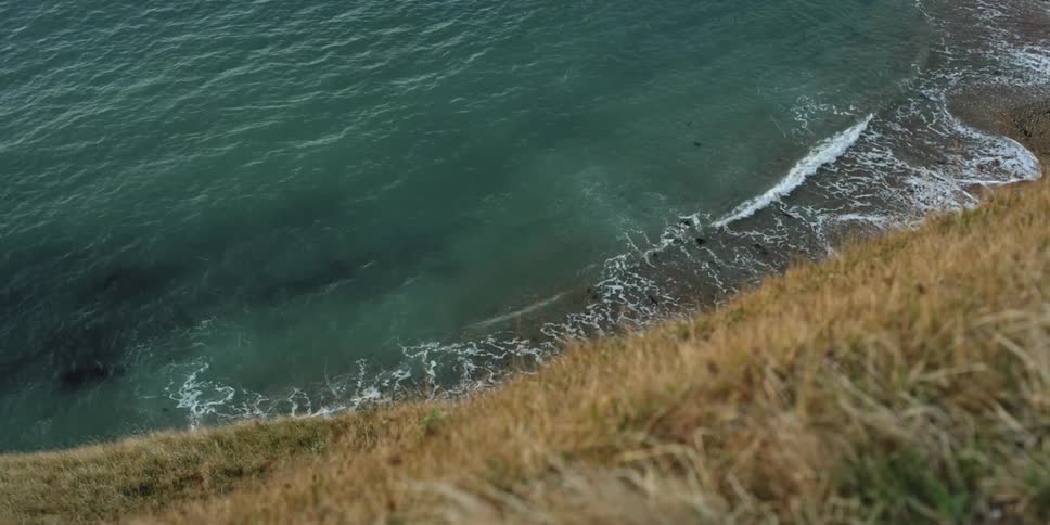Waves crash on a shore that is overlooked by steep grasslands