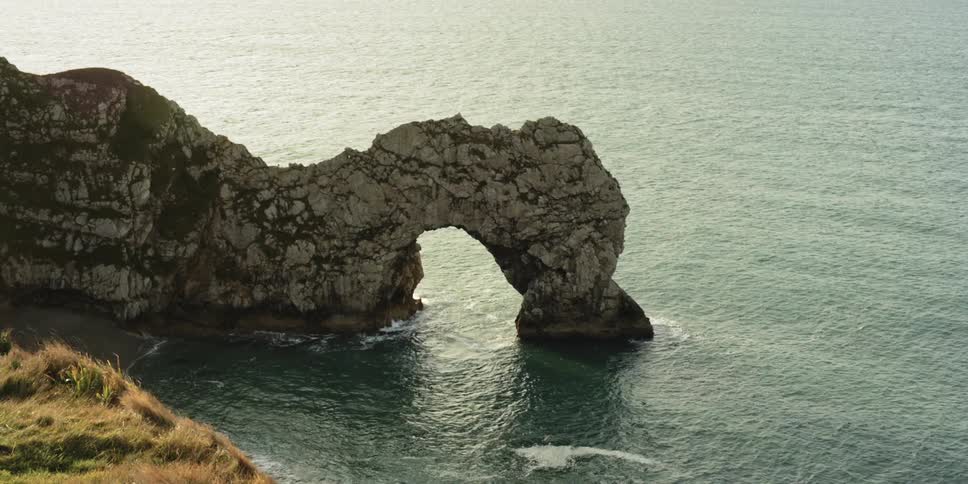 A rocky cliff by the shore with grass in the foreground