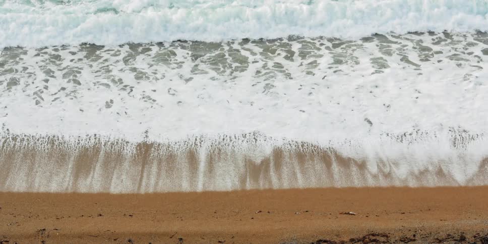 The large waves foam up on the sand