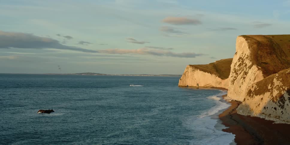 Ocean waves lap a beach overlooked by cliffs as the sun rises