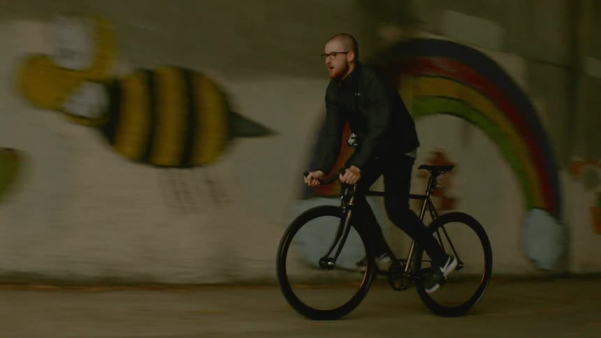 A man is riding a bike on a sidewalk passing graffiti in a tunnel