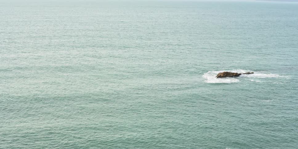 Waves splash on and over a rock in the ocean