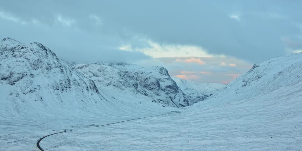 Snow covered land and mountains sit under the cloudy sky