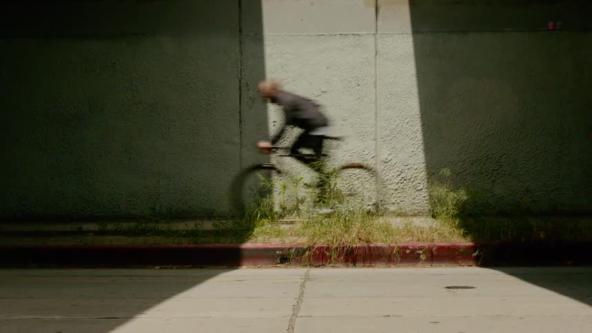A car and a man on a bike travel through a sliver of light under the bridge