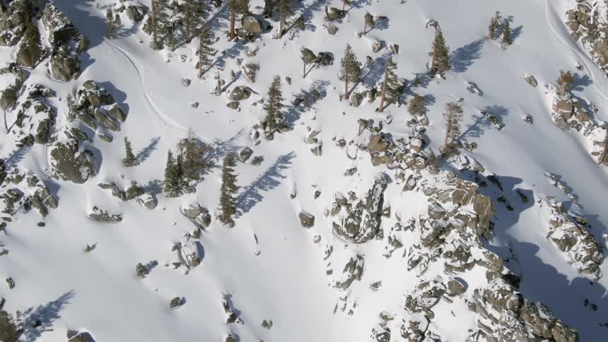 A skier goes down a trail next to a mountain ridge on fresh powder