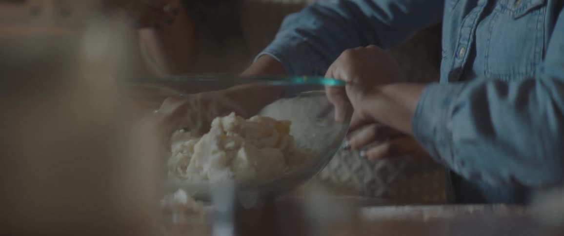 A woman teaching a girl how to knead dough inside a glass bowl