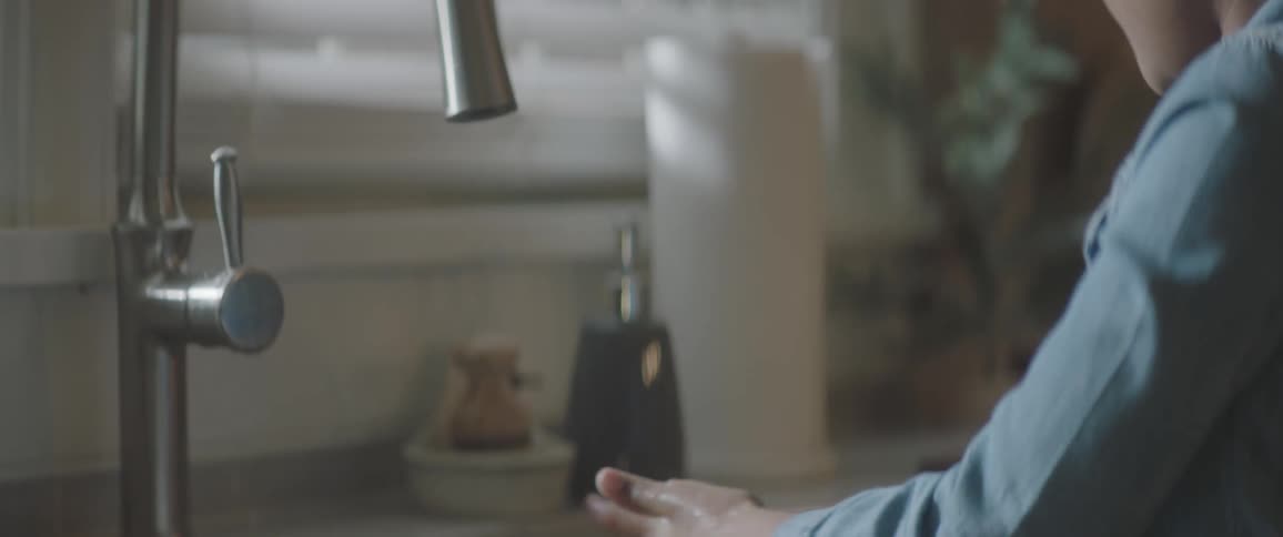 A boy washes his hands at the sink and then dries off with a paper towel