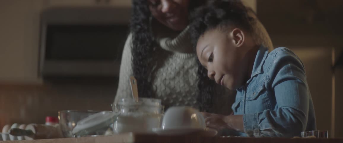 Black woman helps black girl cook in the kitchen during daylight