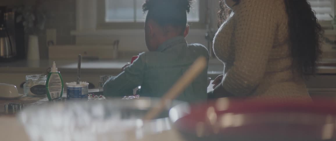 A young girl decorates cookies while a woman watches her