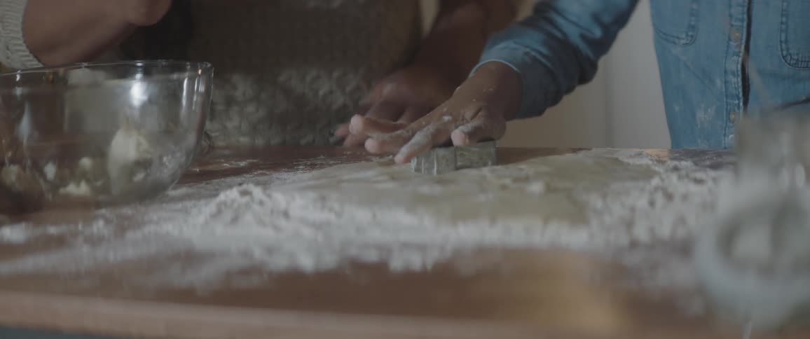 Woman and child use cookie cutters on the dough in preparation to bake cookies