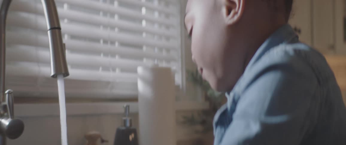 A young black girl is washing her hands in the kitchen sink with a goose neck faucet