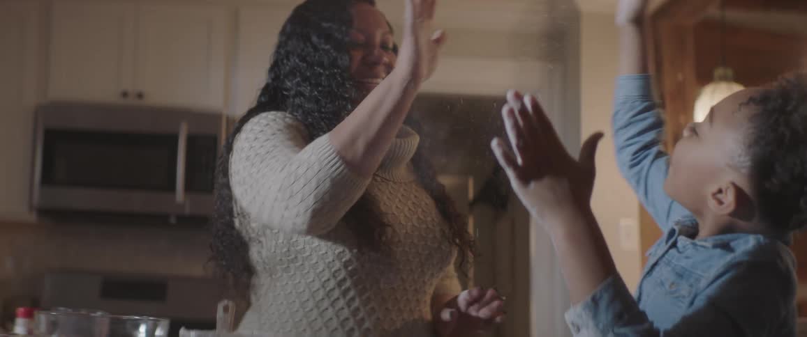 Daughter giving her mother a high five while baking cookies in the kitchen