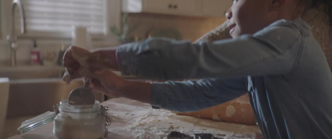 A young girl sprinkles flour on some dough