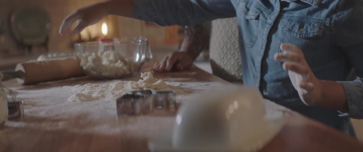 A young boy is helping his mother roll dough on the counter