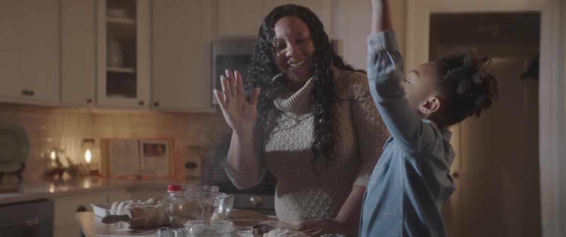 A mother and daughter high five each other standing in the kitchen