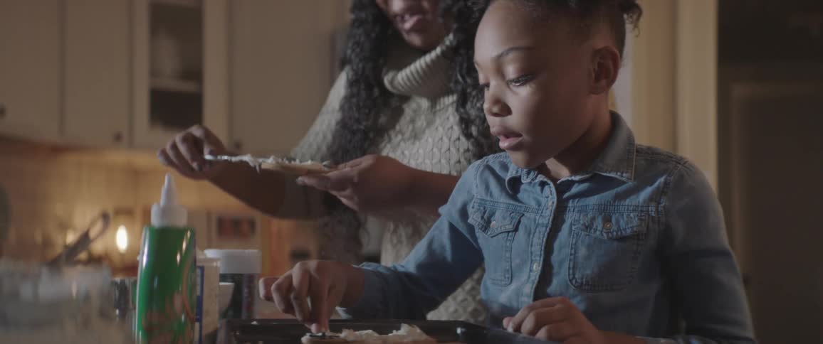 A woman and a little girl decorate cookies