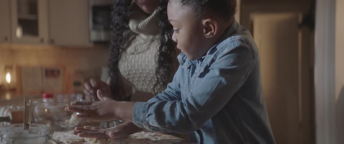 A girl presses down and flattens cookie dough on the counter while her mom watches