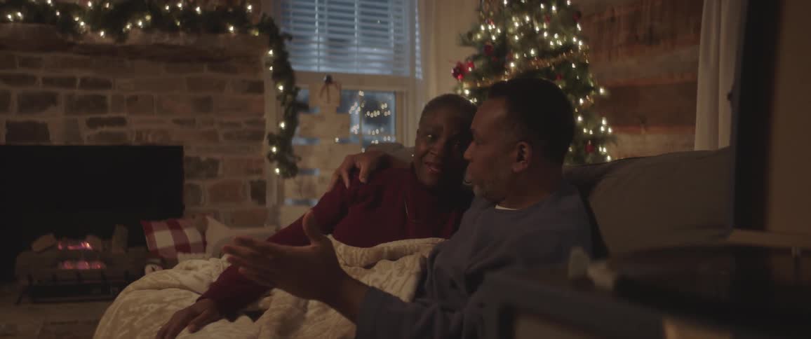 Senior black man and woman under blanket sit on the couch next to the christmas tree at home